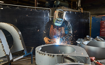 Technician welding components for high-pressure industrial blowers in AF1 workshop